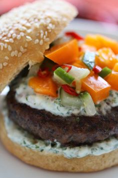 a hamburger with vegetables on it sitting on top of a white plate next to a bun