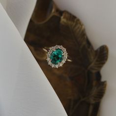 an emerald and diamond ring sitting on top of a white cloth