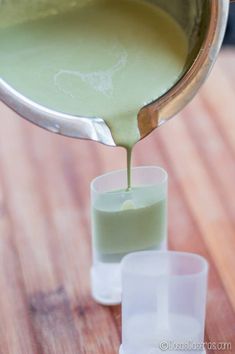 someone pouring something into small cups on a wooden table