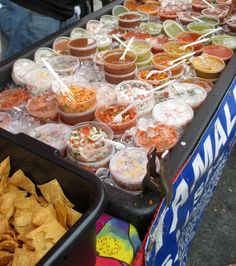 many different kinds of food in containers on a table with chips and dips next to each other