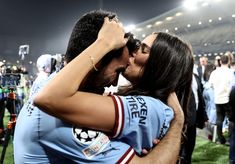 a man and woman kissing in front of a crowd at a soccer game on the field