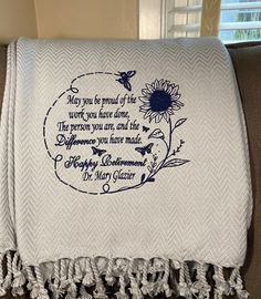 a white towel with an embroidered quote on it sitting on top of a couch next to a window