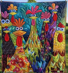 a quilted wall hanging in the grass with three chickens on it's sides