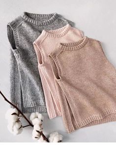 two sweaters are sitting next to cotton flowers on a white surface, one is pink and the other is grey