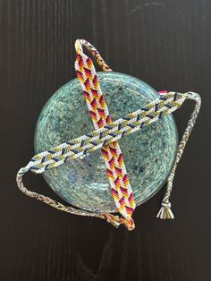 two braided bracelets sitting on top of a glass bowl with a tassel