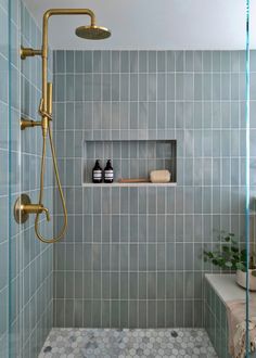 a bathroom with blue tiled walls and gold fixtures, including a shower head and shelves