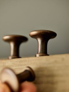 a close up of two knobs on a wooden surface with a person's hand