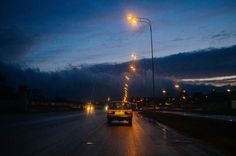 a car driving down the road at night with its headlights on and street lights lit up