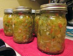 three jars filled with pickles sitting on top of a pink towel