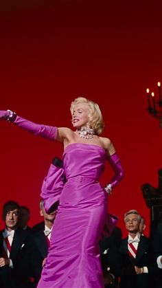 a woman in a purple dress is dancing with other people behind her and on the red background