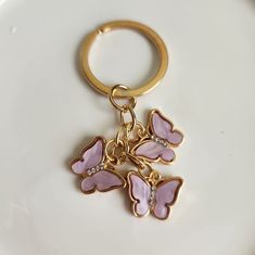 a pink butterfly keychain sitting on top of a white plate next to a gold ring