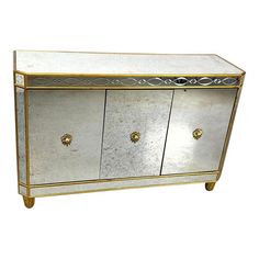 a mirrored cabinet with gold trimmings on the doors and drawers, against a white background