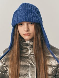 a woman with long hair wearing a silver jacket and a blue knitted beanie