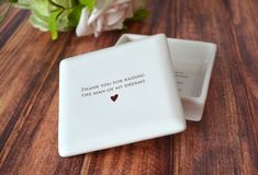 a small white box sitting on top of a wooden table next to a bouquet of flowers