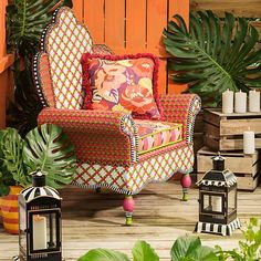 a colorful chair sitting on top of a wooden floor next to potted plants and lanterns