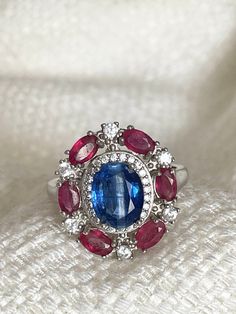 Beautiful vintage look oval top rich blue Nepal kyanite, red ruby and cubic zirconia ring.  14K white gold plated over 925 sterling silver US size: 8 Stones: 8.7 x 7mm; 4 x 3mm and 2mm Face ring: 19.5 x 17.5 mm R743 Oval Cubic Zirconia Gemstones For Anniversary, Red Sapphire Ring With Oval Shape And Accent Stones, Oval Ruby Ring With Cubic Zirconia For Anniversary, Oval Ruby Ring With Cubic Zirconia Center Stone, Oval Ruby Ring Collectible, Vintage Red Oval Ruby Ring, Oval Multi-stone Ruby Ring For Anniversary, Oval Ruby Ring In Cubic Zirconia Fine Jewelry, Oval Ruby Gemstones For Anniversary