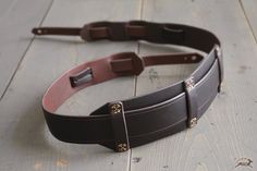 a leather belt with two metal buckles on top of wooden planked flooring