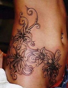 a woman's stomach with flowers and swirls tattooed on the side of her belly