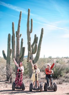 three people on segways in front of a large saguado cactus with their arms up