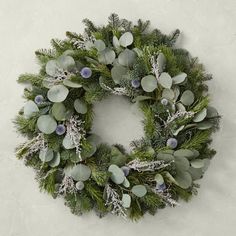 a green wreath with blue berries and greenery hanging on a white wall in the snow