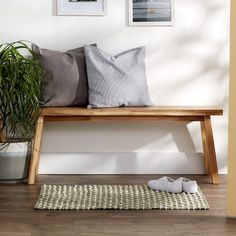 a wooden bench sitting next to a white wall with pictures on the wall above it