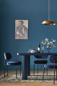 a dining room table with blue chairs and a painting hanging on the wall above it