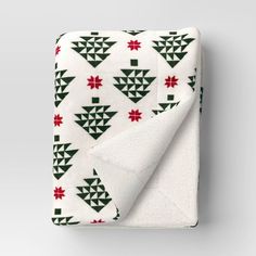 a white blanket with green and red christmas trees on it, folded up to the side