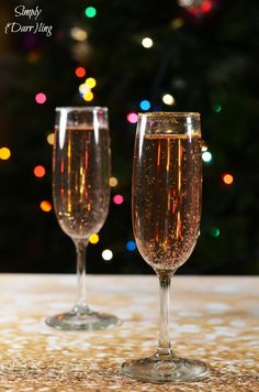 two champagne flutes sitting on top of a table next to a christmas tree with lights in the background