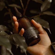 a hand holding a brown bottle in front of some plants and leaves on a dark background