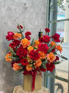 a vase filled with red and orange flowers sitting on top of a table next to a window