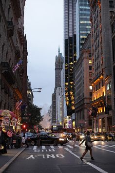 a city street with cars and people walking on the sidewalk at night, in front of tall buildings