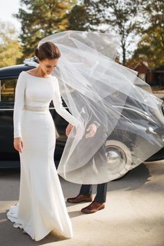 a woman in a white wedding dress standing next to a black car