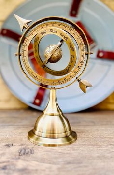 a golden compass on top of a wooden table next to a plate with red and blue plates