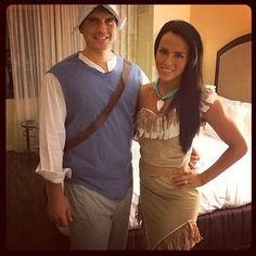 a man standing next to a woman in front of a bed wearing a dress and hat