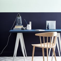 a blue table with two white chairs and a lamp on top of it in front of a black wall