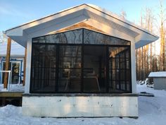 a small white building sitting on top of a snow covered ground next to a forest