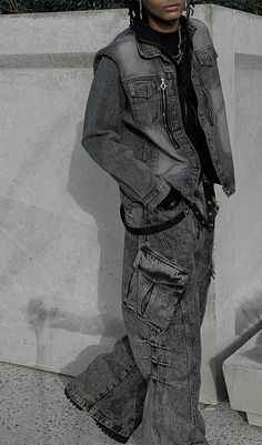 a young man standing in front of a cement wall with his hands on his hips