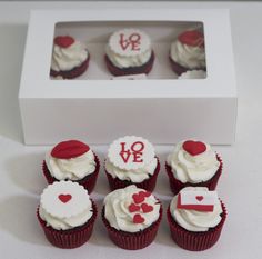 cupcakes with white frosting and red decorations in a box on a table