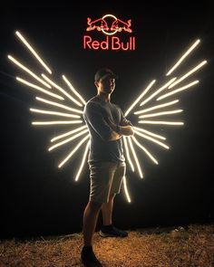 a man standing in front of a red bull sign at night with his arms crossed