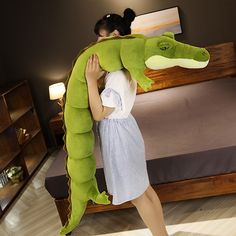 a woman is carrying a large stuffed alligator on her back while standing in front of a bed