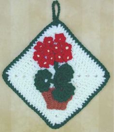 a crocheted pot holder with red flowers on the front and green trim around it