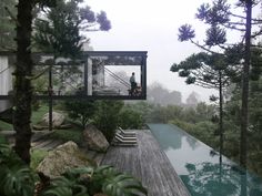 a person standing on the deck of a house overlooking a pool in the middle of trees