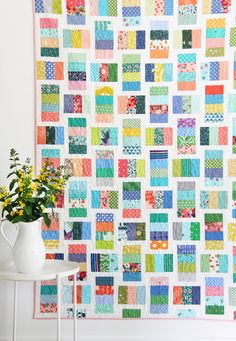 a colorful quilt hanging on the wall next to a white vase with flowers in it