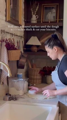 a woman standing in front of a kitchen sink making something on the counter with her hands