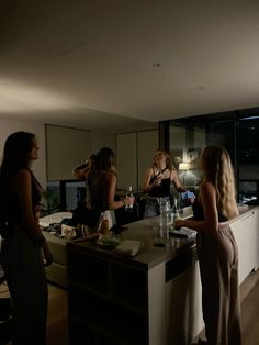 three women standing in a kitchen talking to each other while one woman stands at the counter