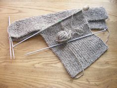 two gray knitted mittens with needles and yarn