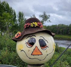 a painted pumpkin with a scarecrow face on it's head, sitting next to a river