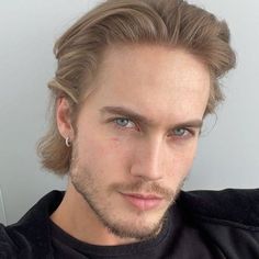 a man with long hair and blue eyes looks at the camera while wearing a black t - shirt