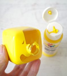 a hand holding a small yellow object next to a bottle