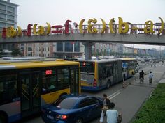 people are walking on the sidewalk next to buses and cars in front of an overpass